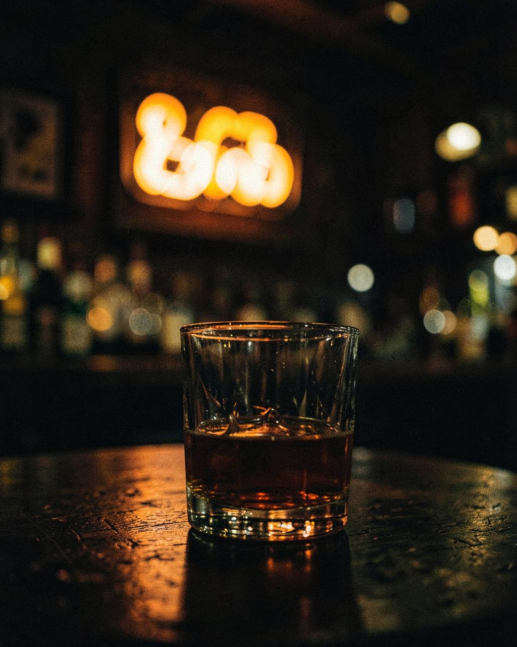 Whiskey glass glowing under a neon sign inside a western bar