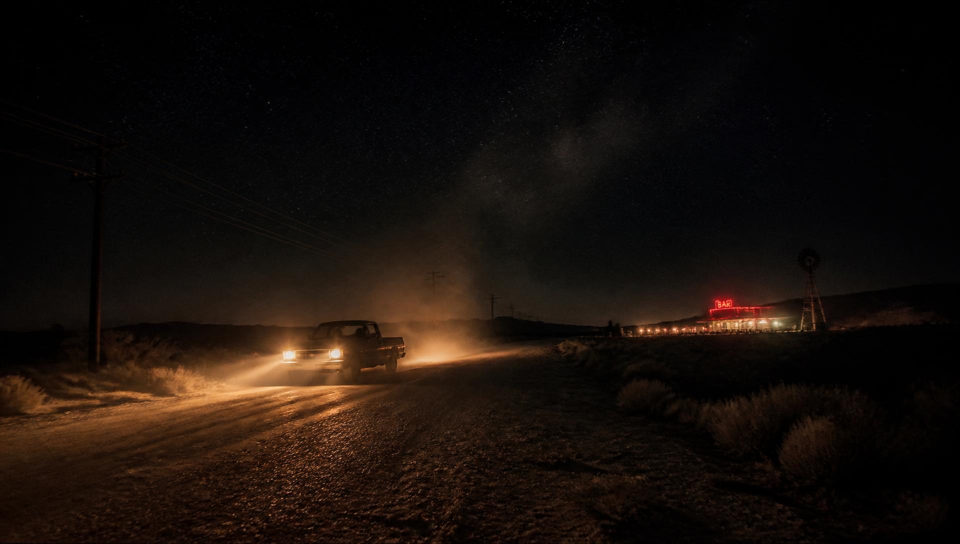 Empty backroad at night lit by pickup truck headlights